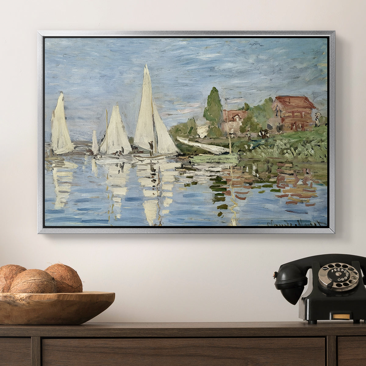 Regatta at Argenteuil, 1872 by Claude Monet in a silver floater framed canvas displayed above a console table in a hallway, featuring a dynamic nautical scene with boats moving across river.