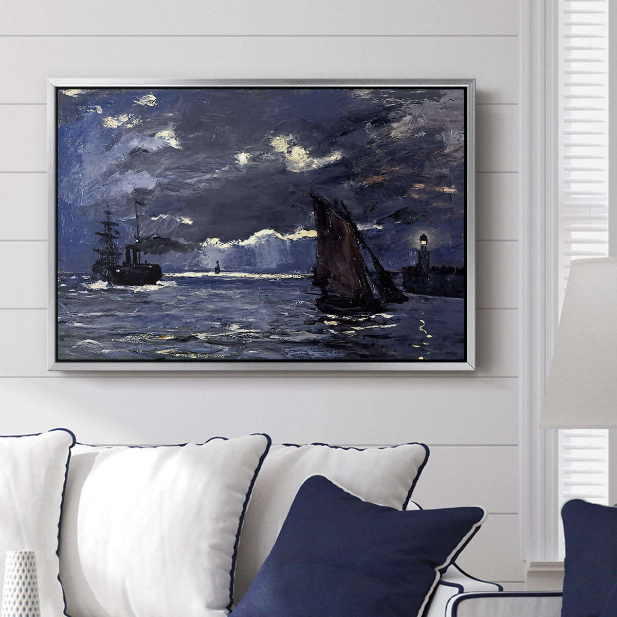 A Seascape, Shipping by Moonlight, 1864 by Claude Monet displayed above a sofa in a living room in a silver floater frame, featuring a nocturnal seascape with boats silhouetted against glowing moon.