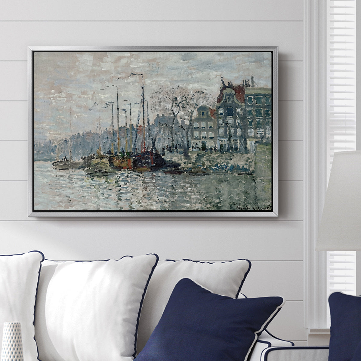 View of the Prins Hendrikkade and Kromme Waal in Amsterdam, 1874 by Claude Monet displayed above a sofa in a living room in a silver floater frame, featuring an impressionist cityscape of canal with ships and architecture.