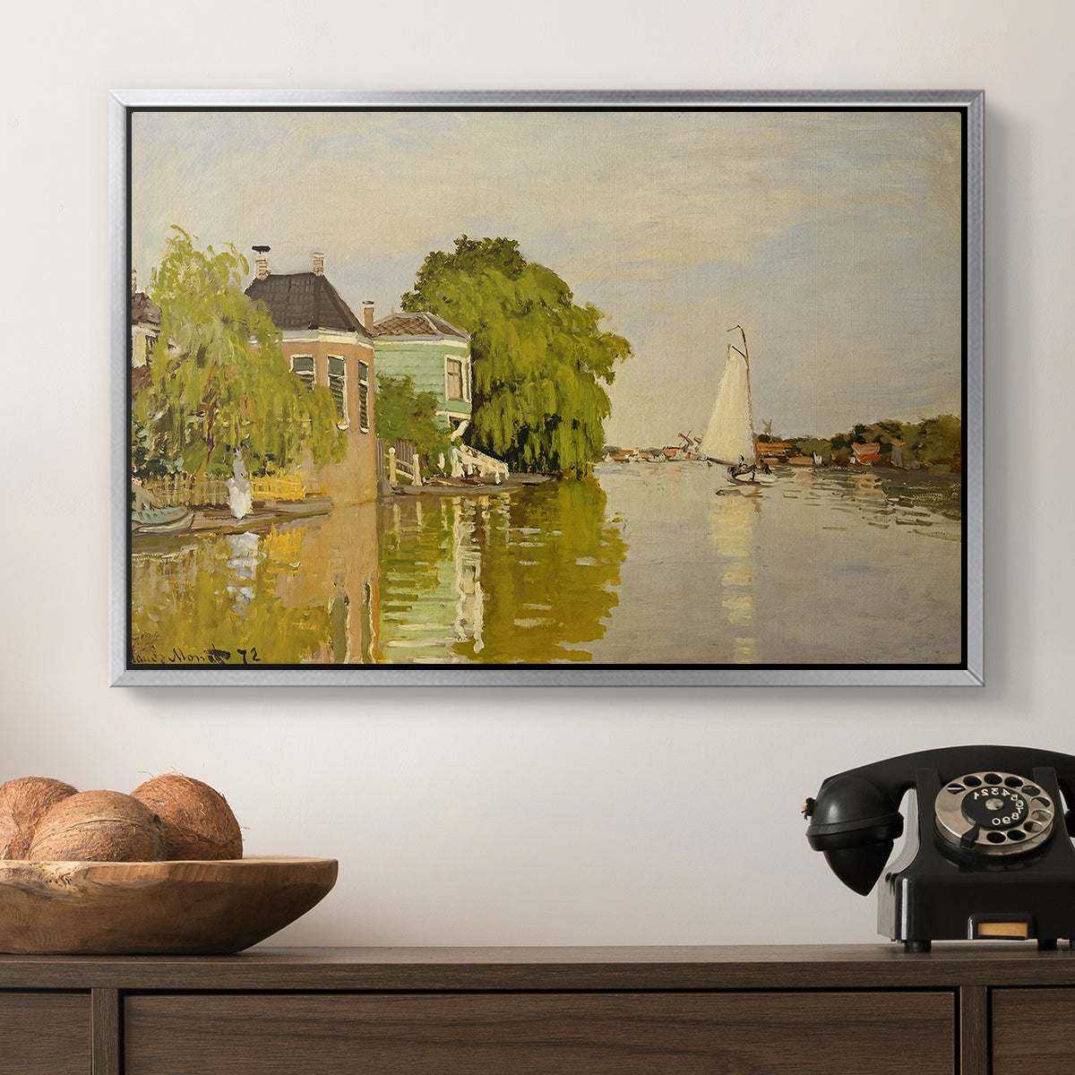 Houses on the Achterzaan, 1871 by Claude Monet in a silver floater framed canvas displayed above a console table in a hallway, featuring a peaceful village scene with houses bordering water.