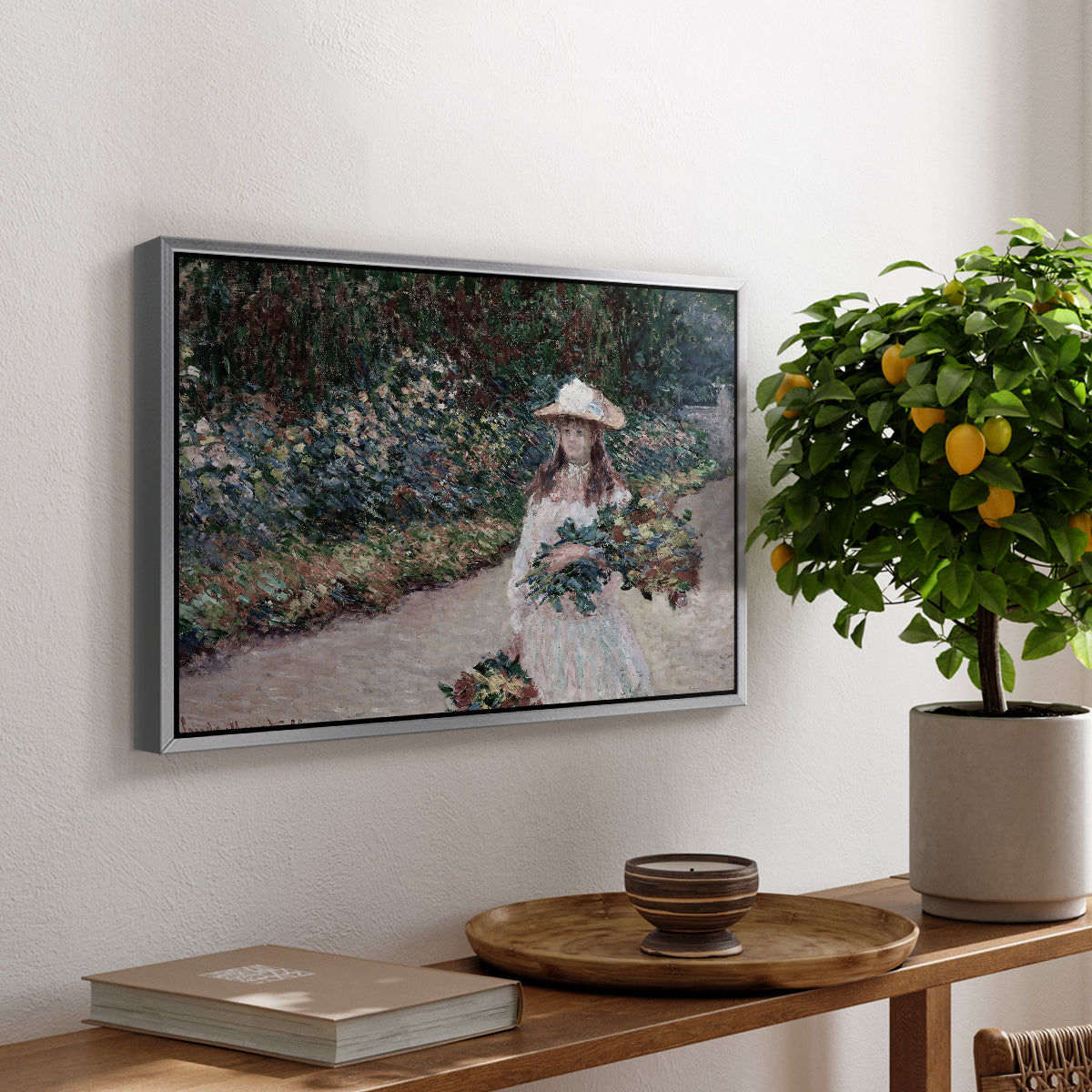 Young Girl in the Garden at Giverny, 1888 by Claude Monet, presented in a silver floater framed canvas featuring a young girl seated in lush garden surrounded by blooming flowers, displayed above a hallway console table.