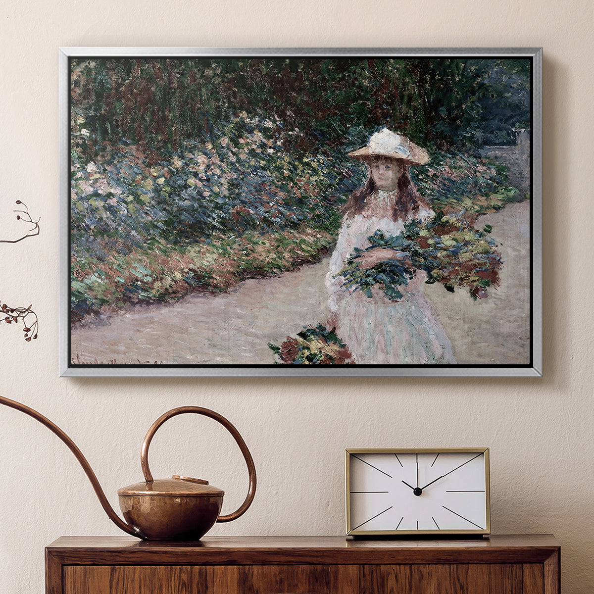 Silver floater framed canvas featuring a figure resting in colorful garden under soft light, displayed above a cabinet in a soft-toned living room.
