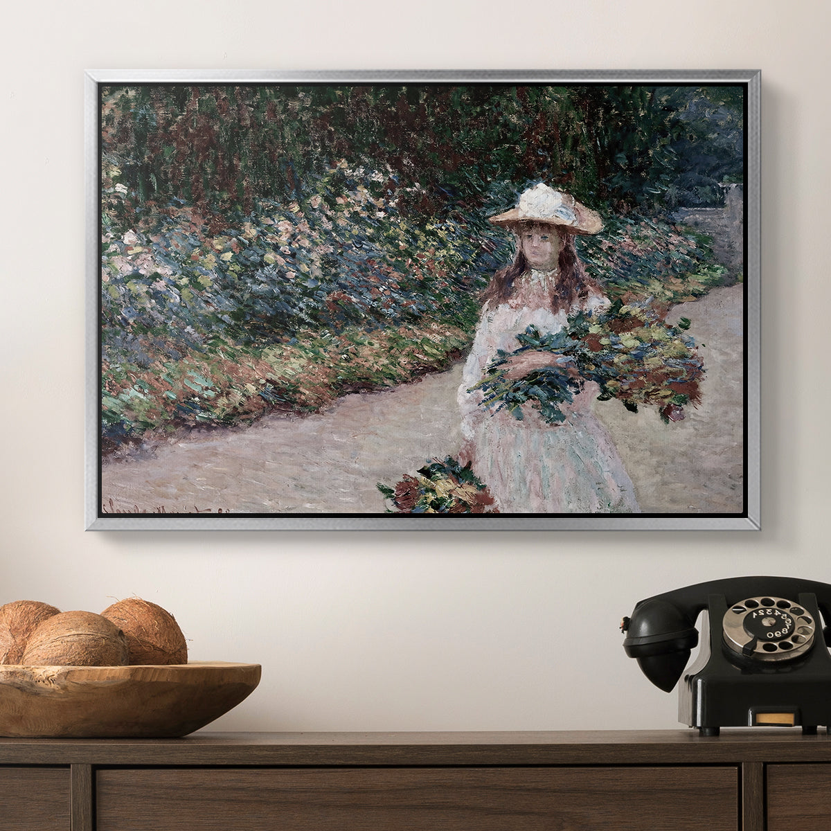 Young Girl in the Garden at Giverny, 1888 by Claude Monet in a silver floater framed canvas displayed above a console table in a hallway, featuring a tranquil outdoor portrait of girl in floral setting.