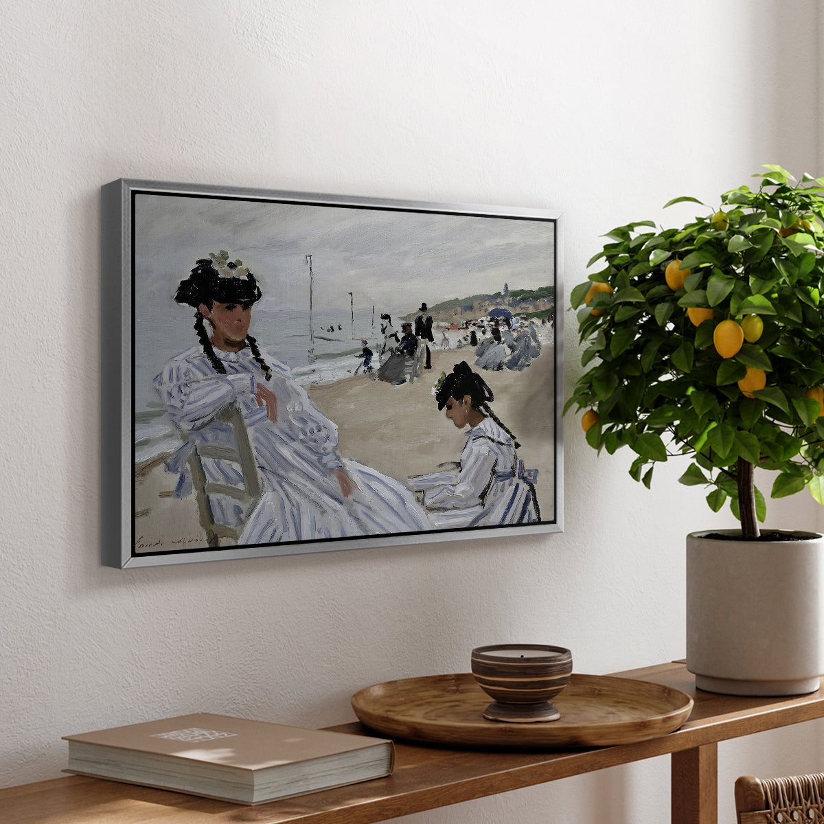 On the Beach at Trouville, 1870 by Claude Monet, presented in a silver floater framed canvas featuring figures seated on beach with parasols facing the ocean, displayed above a hallway console table.