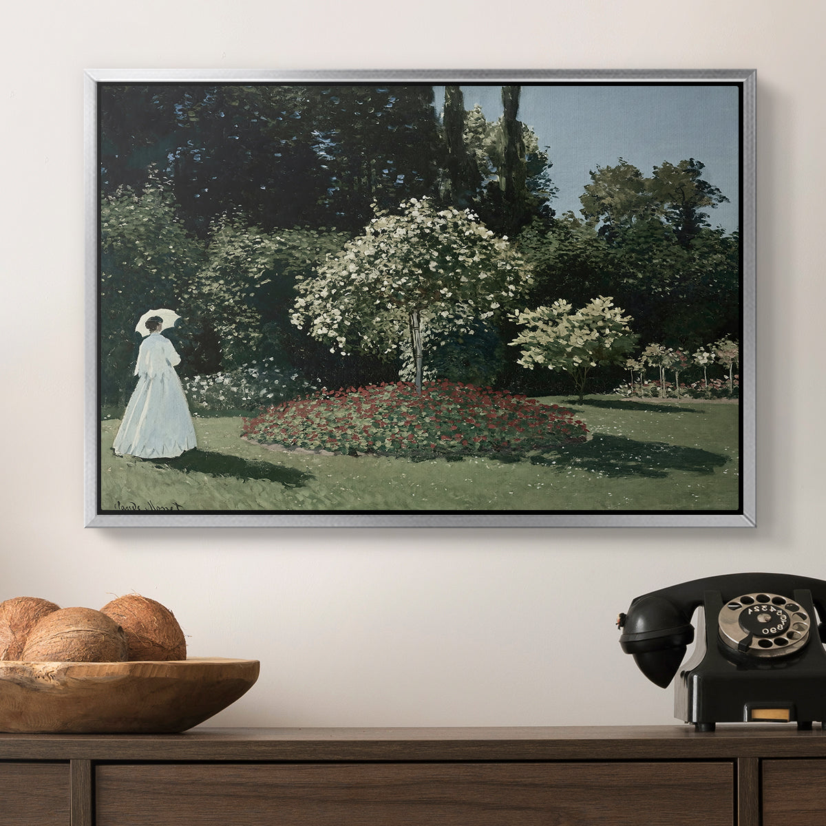 Woman in the Garden, Sainte-Adresse, 1867 by Claude Monet in a silver floater framed canvas displayed above a console table in a hallway, featuring a tranquil garden portrait with soft natural light.