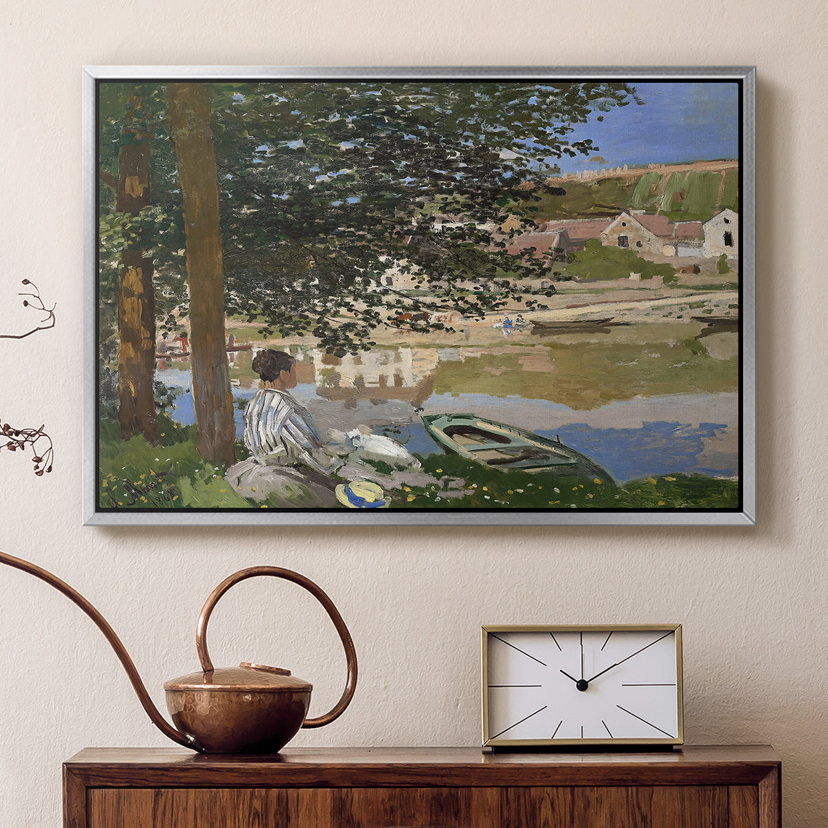 Silver floater framed canvas featuring an impressionist landscape with people relaxing along the Seine, displayed above a cabinet in a soft-toned living room.
