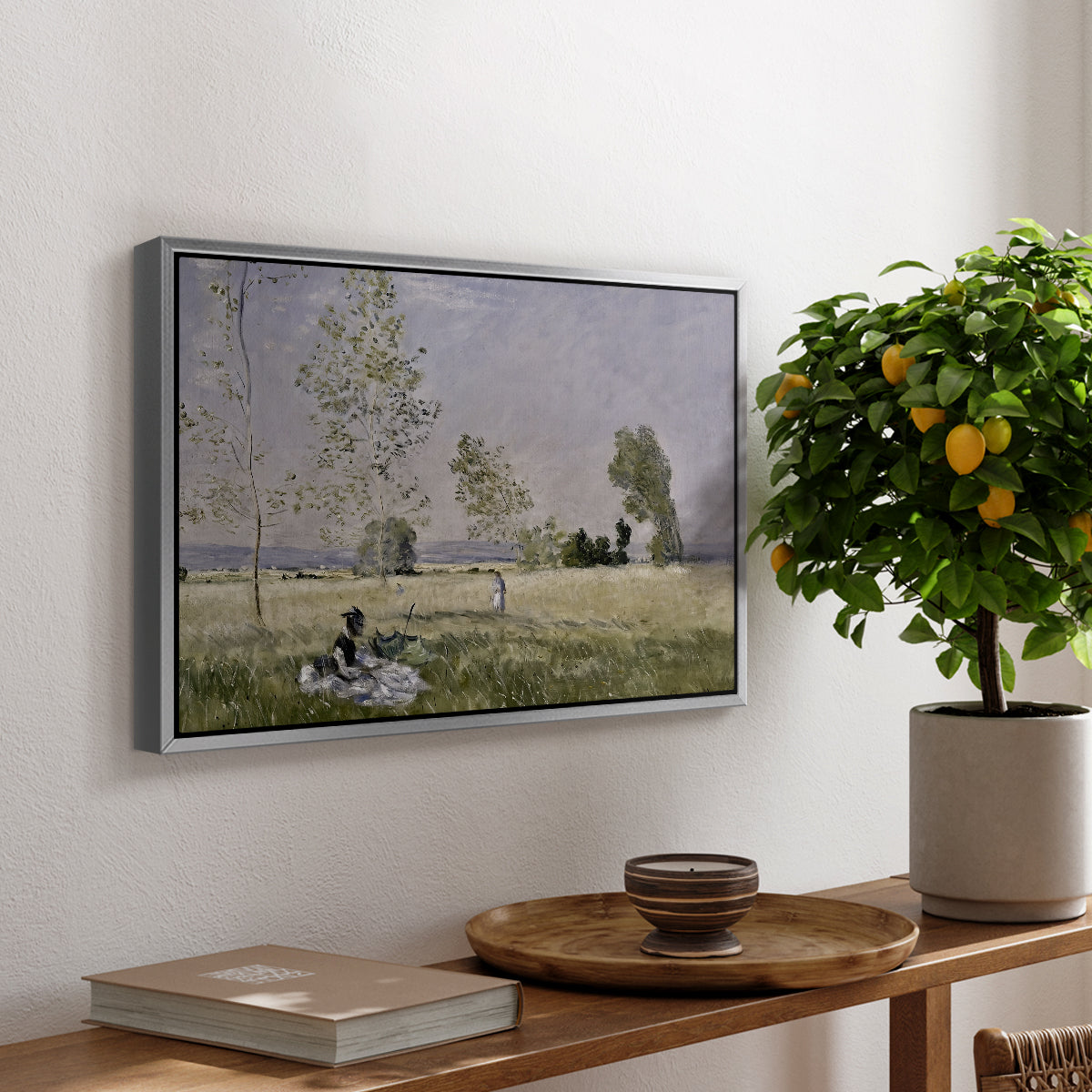 Summer (L'ete), 1874 by Claude Monet, presented in a silver floater framed canvas featuring a woman seated in grassy field beneath tree in bright summer landscape, displayed above a hallway console table.