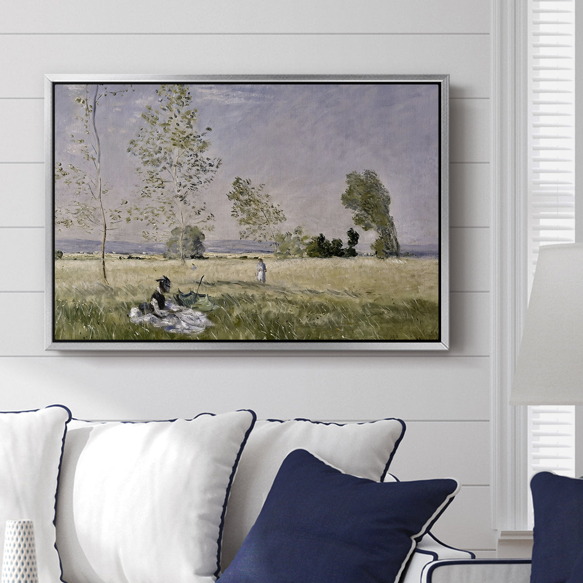Summer (L'ete), 1874 by Claude Monet displayed above a sofa in a living room in a silver floater frame, featuring an impressionist countryside scene with figure resting in shade.