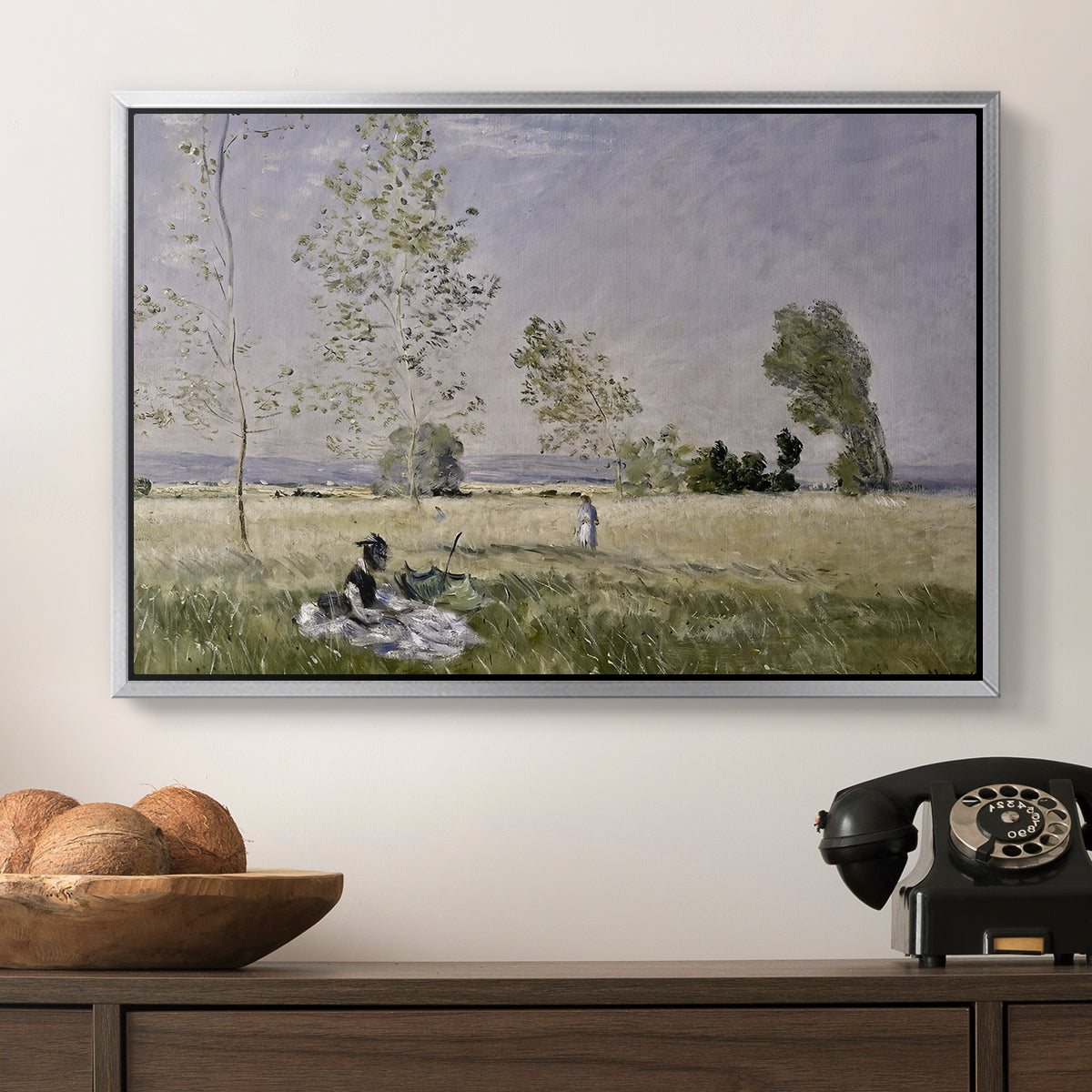 Summer (L'ete), 1874 by Claude Monet in a silver floater framed canvas displayed above a console table in a hallway, featuring a tranquil summer landscape with lone figure in nature.