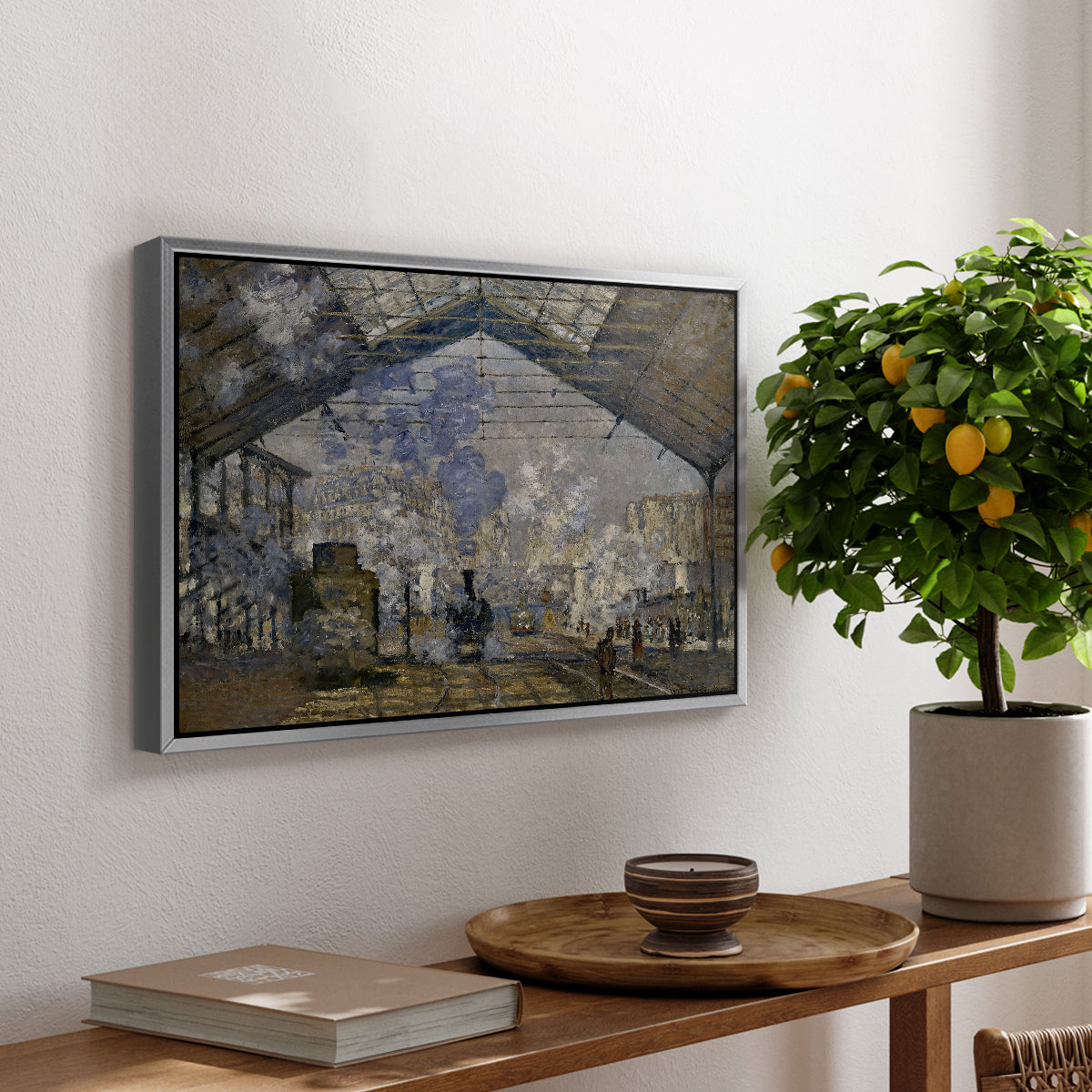 The Gare Saint-Lazare, 1877 by Claude Monet, presented in a silver floater framed canvas featuring a train station interior filled with steam and locomotives under iron structure, displayed above a hallway console table.