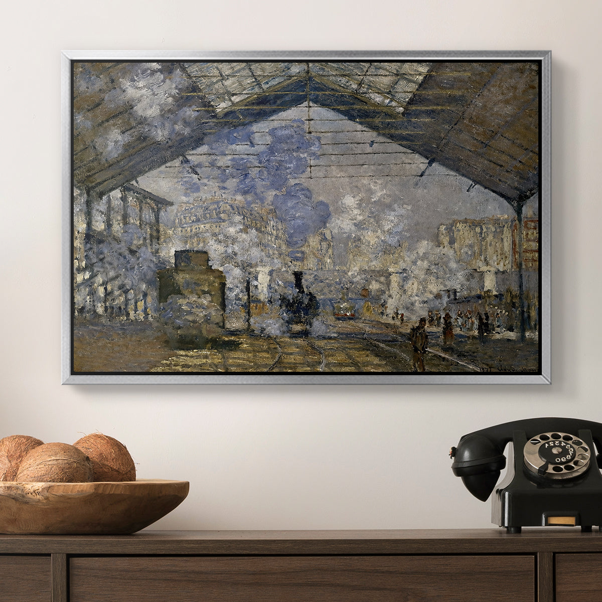 The Gare Saint-Lazare, 1877 by Claude Monet in a silver floater framed canvas displayed above a console table in a hallway, featuring a bustling transport hub with trains beneath glass roof.