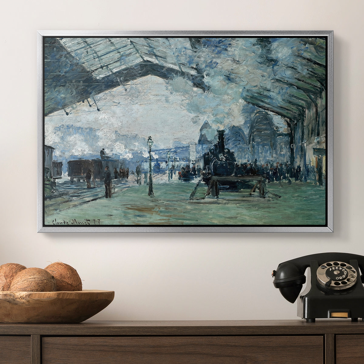 The Saint-Lazare Station, 1877 by Claude Monet in a silver floater framed canvas displayed above a console table in a hallway, featuring a dramatic depiction of industrial space with trains and light.