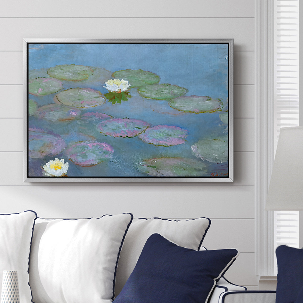 Water Lilies (Nymphéas), 1897-1899 by Claude Monet displayed above a sofa in a living room in a silver floater frame, featuring an impressionist pond scene with lily pads and soft reflections.