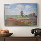 Tulip Fields with the Rijnsburg Windmill, 1886 by Claude Monet in a silver floater framed canvas displayed above a console table in a hallway, featuring a rural scene with patterned rows of flowers and windmill.