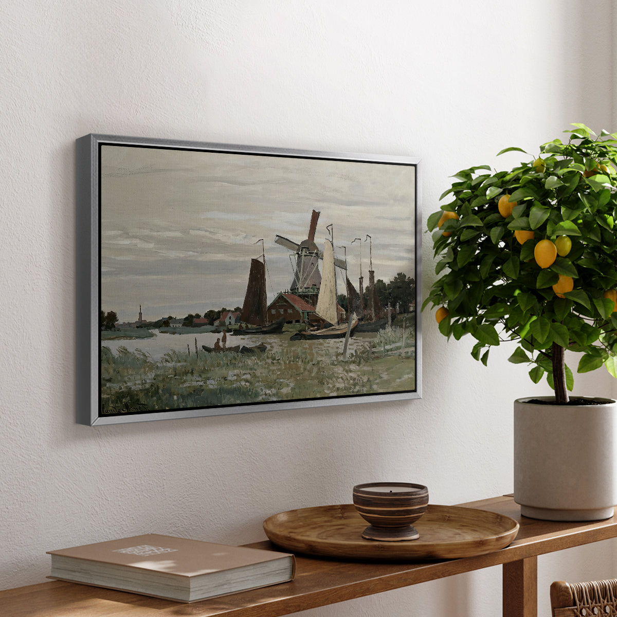 Windmill at Zaandam, 1871 by Claude Monet, presented in a silver floater framed canvas featuring a single windmill beside water with surrounding buildings and sky, displayed above a hallway console table.