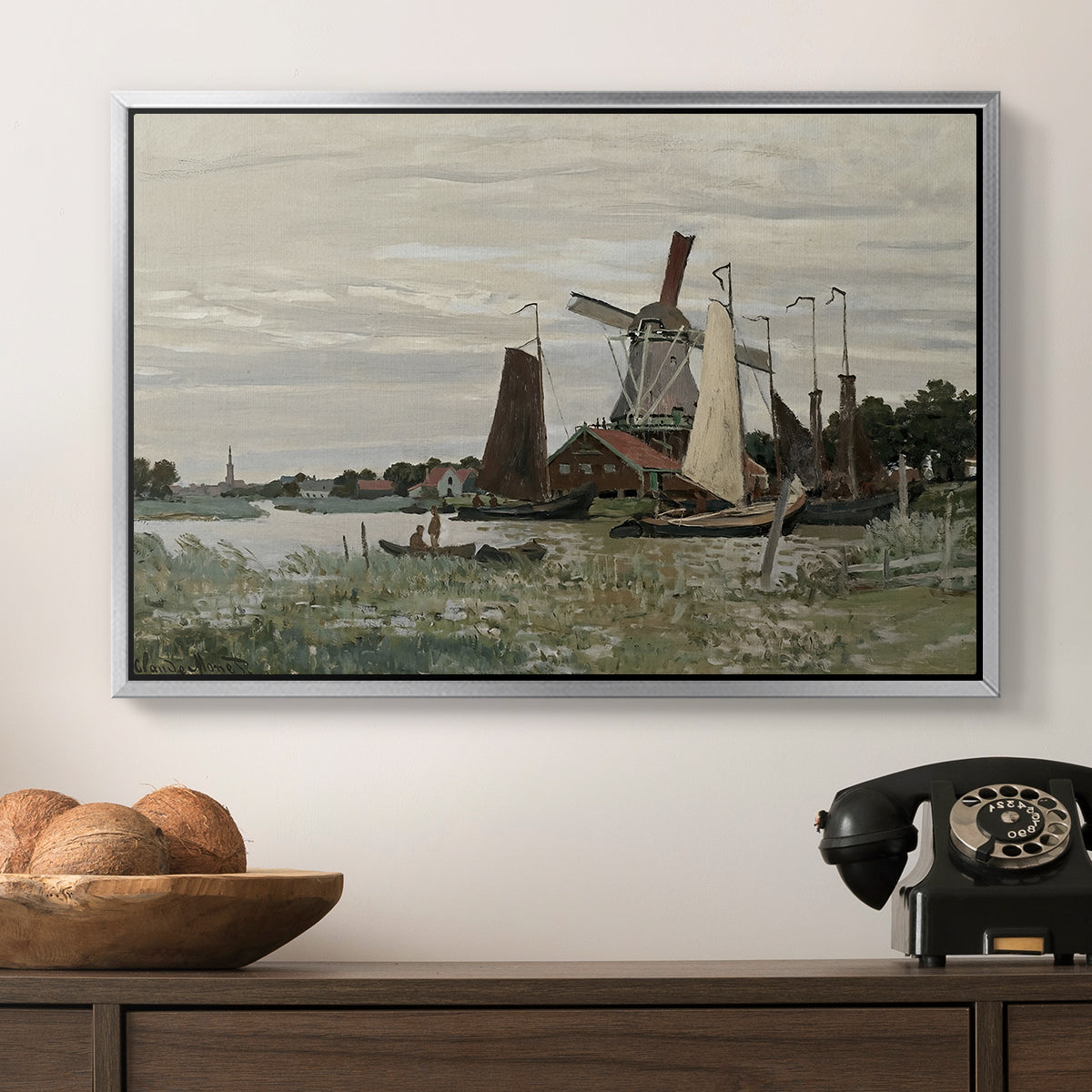 Windmill at Zaandam, 1871 by Claude Monet in a silver floater framed canvas displayed above a console table in a hallway, featuring a countryside structure standing against open sky.