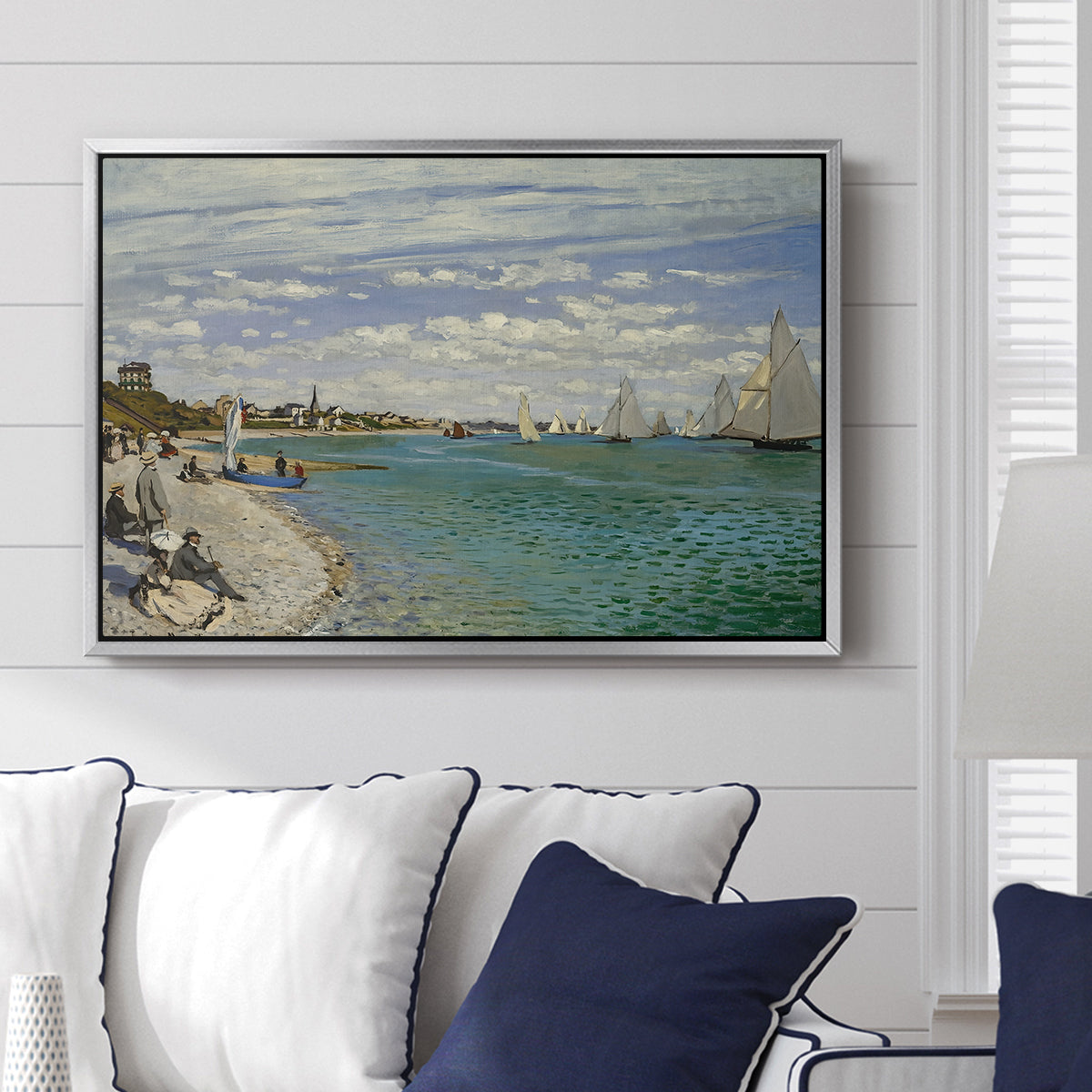 Regatta at Sainte-Adresse, 1867 by Claude Monet displayed above a sofa in a living room in a silver floater frame, featuring a lively regatta scene with boats and people on beach.
