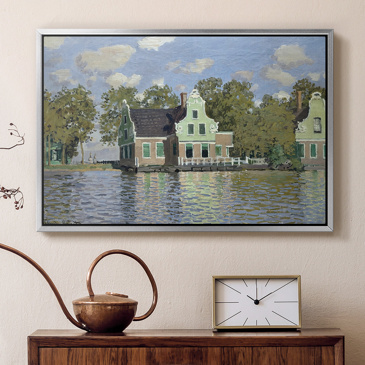 Silver floater framed canvas featuring a peaceful canal scene with houses mirrored in water, displayed above a cabinet in a soft-toned living room.