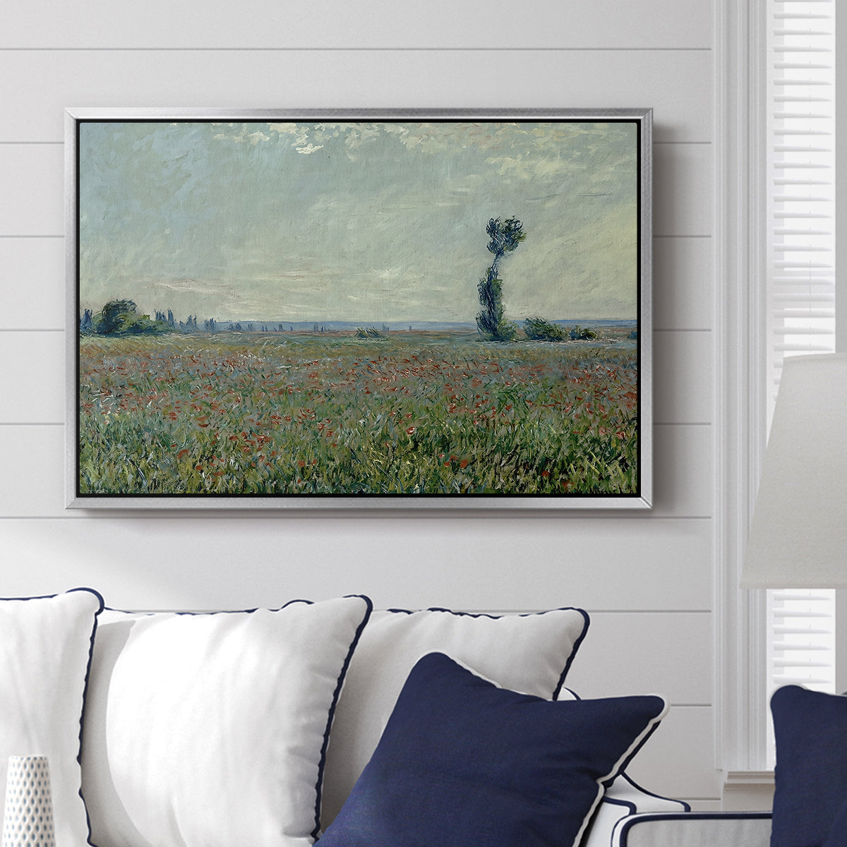 Poppy Field, 1881 by Claude Monet displayed above a sofa in a living room in a silver floater frame, featuring an impressionist landscape filled with blooming flowers and greenery.