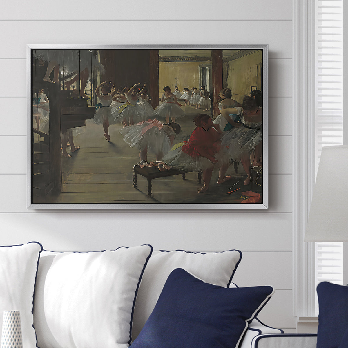 The Dance Class, c. 1873 by Edgar Degas displayed above a sofa in a living room in a silver floater frame, featuring a rehearsal scene with dancers stretching and posing indoors.