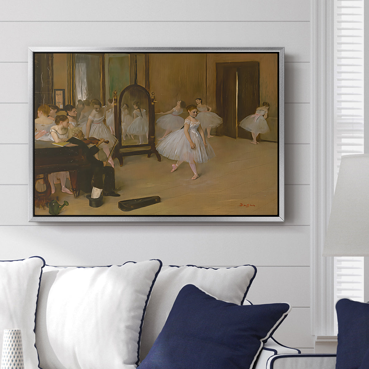 The Dancing Class, c. 1870 by Edgar Degas displayed above a sofa in a living room in a silver floater frame, featuring a rehearsal scene with ballerinas in tutus arranged in studio.
