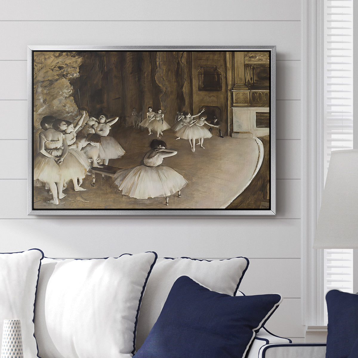 The Rehearsal of the Ballet Onstage, 1874 by Edgar Degas displayed above a sofa in a living room in a silver floater frame, featuring a stage rehearsal scene with dancers preparing performance.
