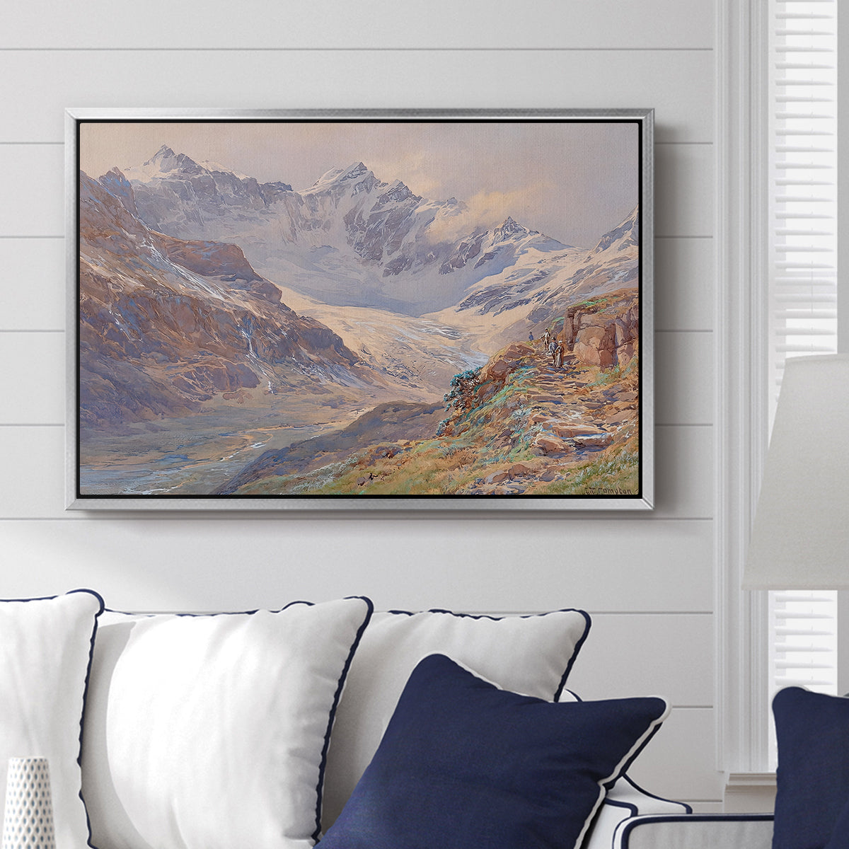 Odenwinklkees with the Johannisberg, 1902 by Edward Theodore Compton displayed above a sofa in a living room in a silver floater frame, featuring a mountain scene with glacier stretching through rocky valley.