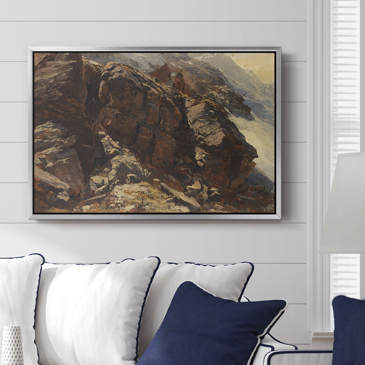 High Mountain Study, c. 1870 by Edward Theodore Compton displayed above a sofa in a living room in a silver floater frame, featuring a detailed study of rugged mountain landscape with sharp contours.