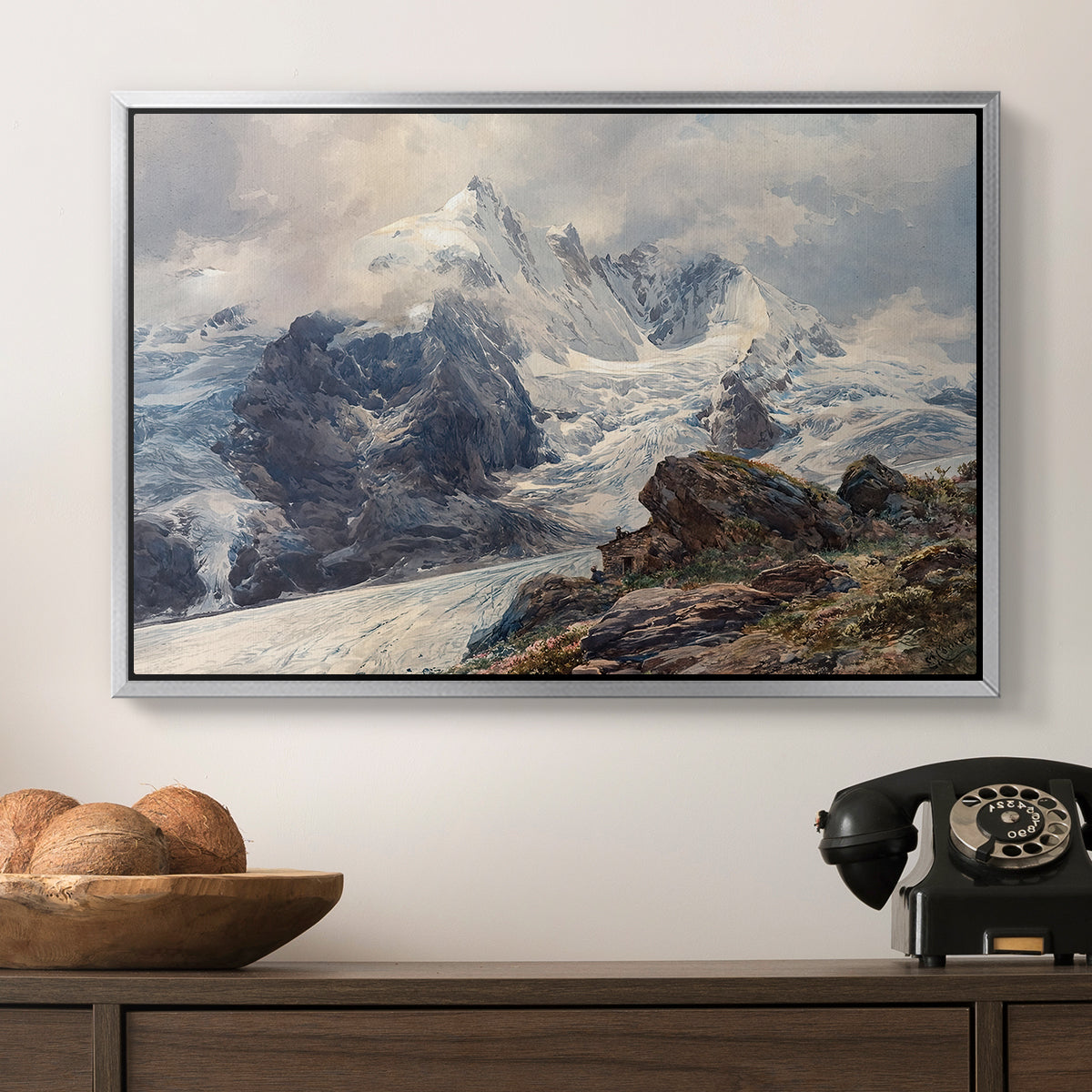 The Grossglockner, 1880 by Edward Theodore Compton in a silver floater framed canvas displayed above a console table in a hallway, featuring an alpine peak dominating surrounding terrain.
