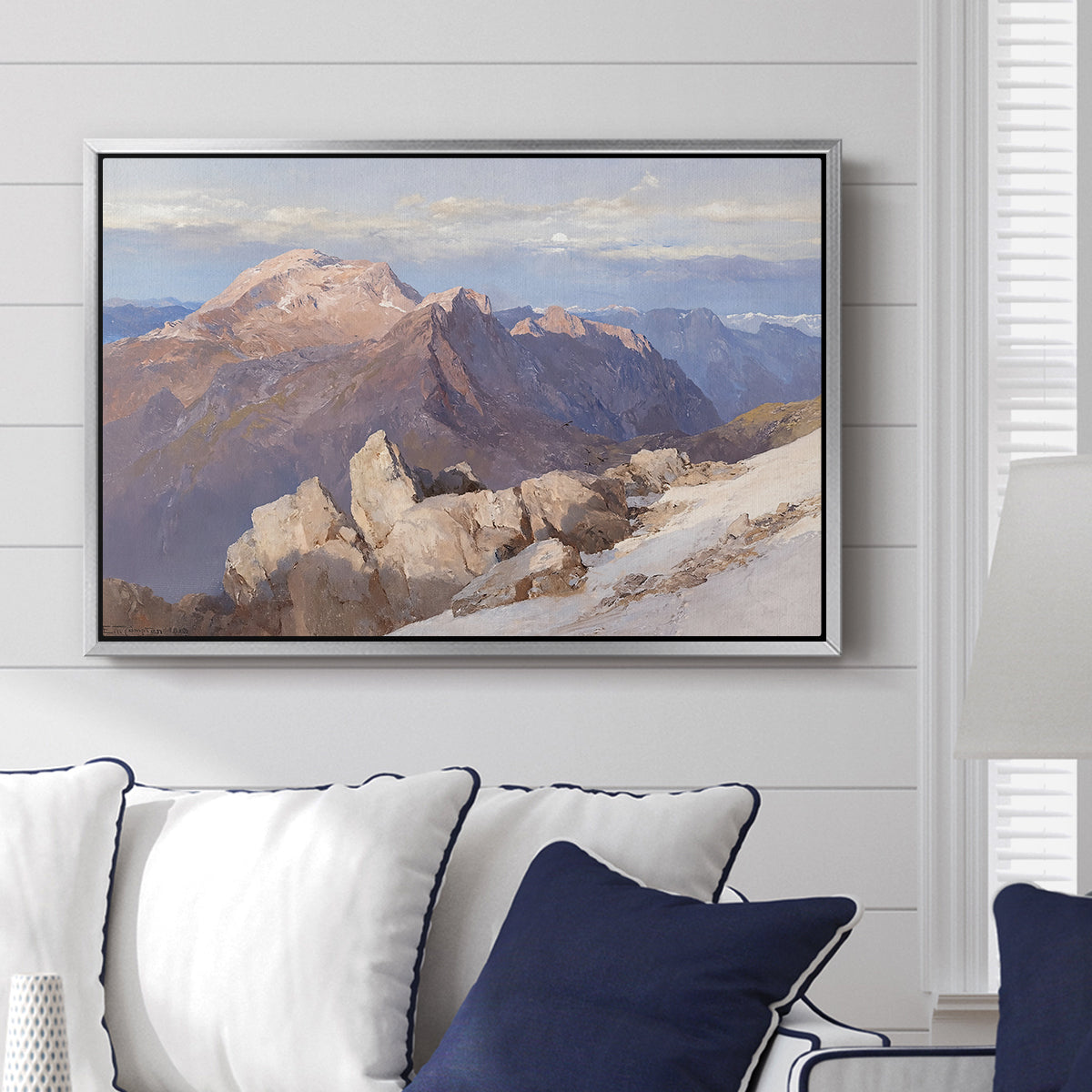 Hoher Göll from Watzmann-Hocheck, 1919 by Edward Theodore Compton displayed above a sofa in a living room in a silver floater frame, featuring an alpine panorama showing layered peaks and valleys.