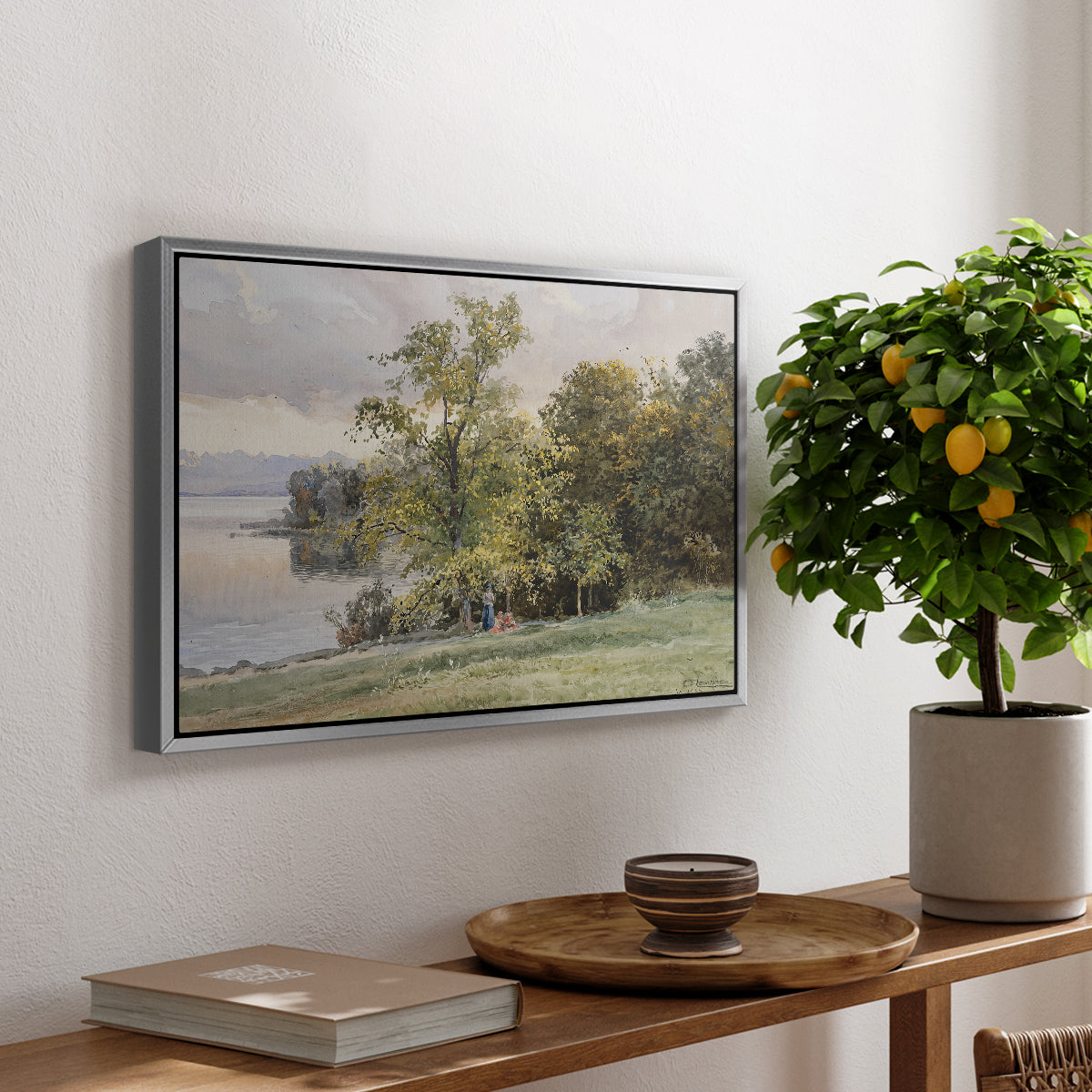 Landscape at Lake Starnberg, 1890 by Edward Theodore Compton, presented in a silver floater framed canvas featuring a lakeside landscape with calm water and trees along shoreline, displayed above a hallway console table.