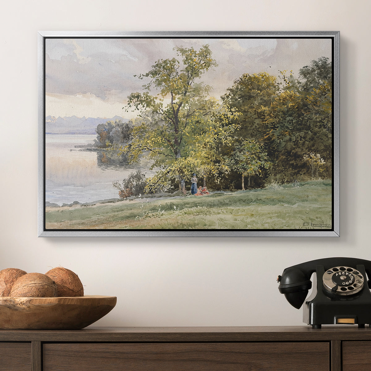 Landscape at Lake Starnberg, 1890 by Edward Theodore Compton in a silver floater framed canvas displayed above a console table in a hallway, featuring a tranquil lakeside view with soft atmospheric tones.