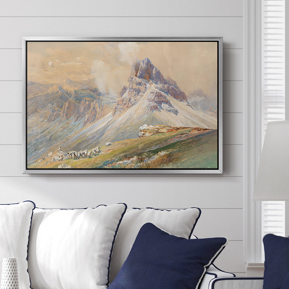 From the Dolomites, 1904 by Edward Theodore Compton displayed above a sofa in a living room in a silver floater frame, featuring an alpine scene with jagged rock formations and distant mountains.