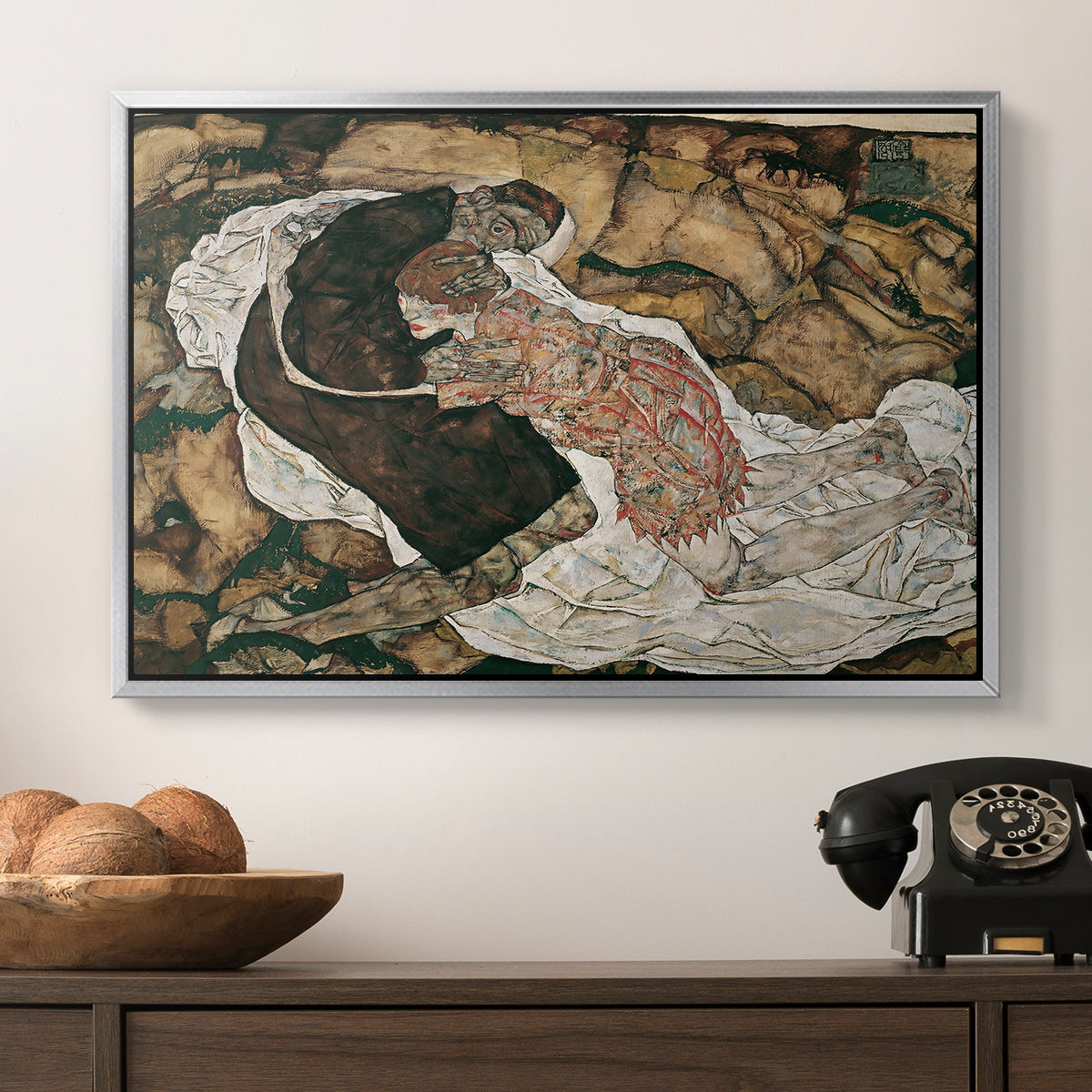 Death and the Maiden, 1915 by Egon Schiele in a silver floater framed canvas displayed above a console table in a hallway, featuring an intense composition exploring life and death through figures.