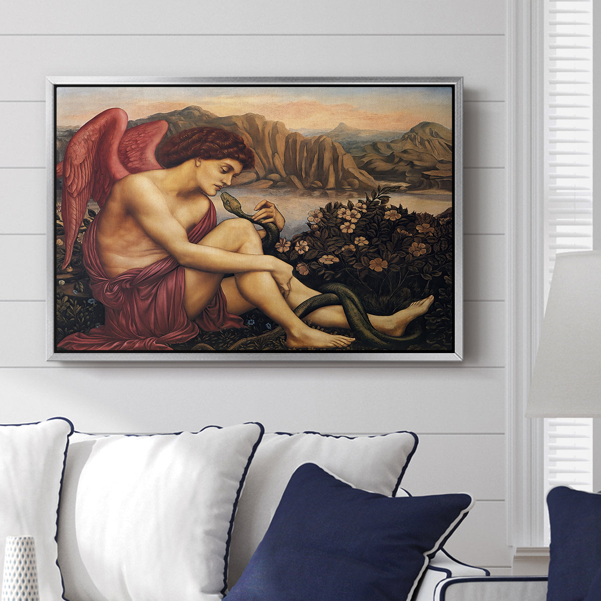 The Angel with the Serpent, c. 1870-1875 by Evelyn De Morgan displayed above a sofa in a living room in a silver floater frame, featuring a winged figure standing over serpent in allegorical composition.