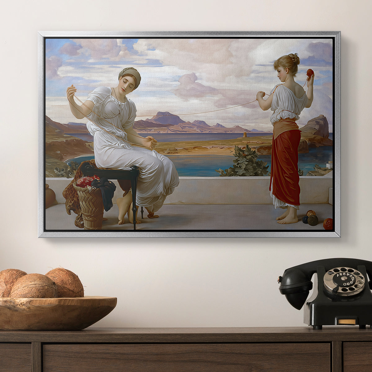 Winding the Skein, c. 1878 by Frederic Leighton in a silver floater framed canvas displayed above a console table in a hallway, featuring an elegant composition of women performing domestic task.