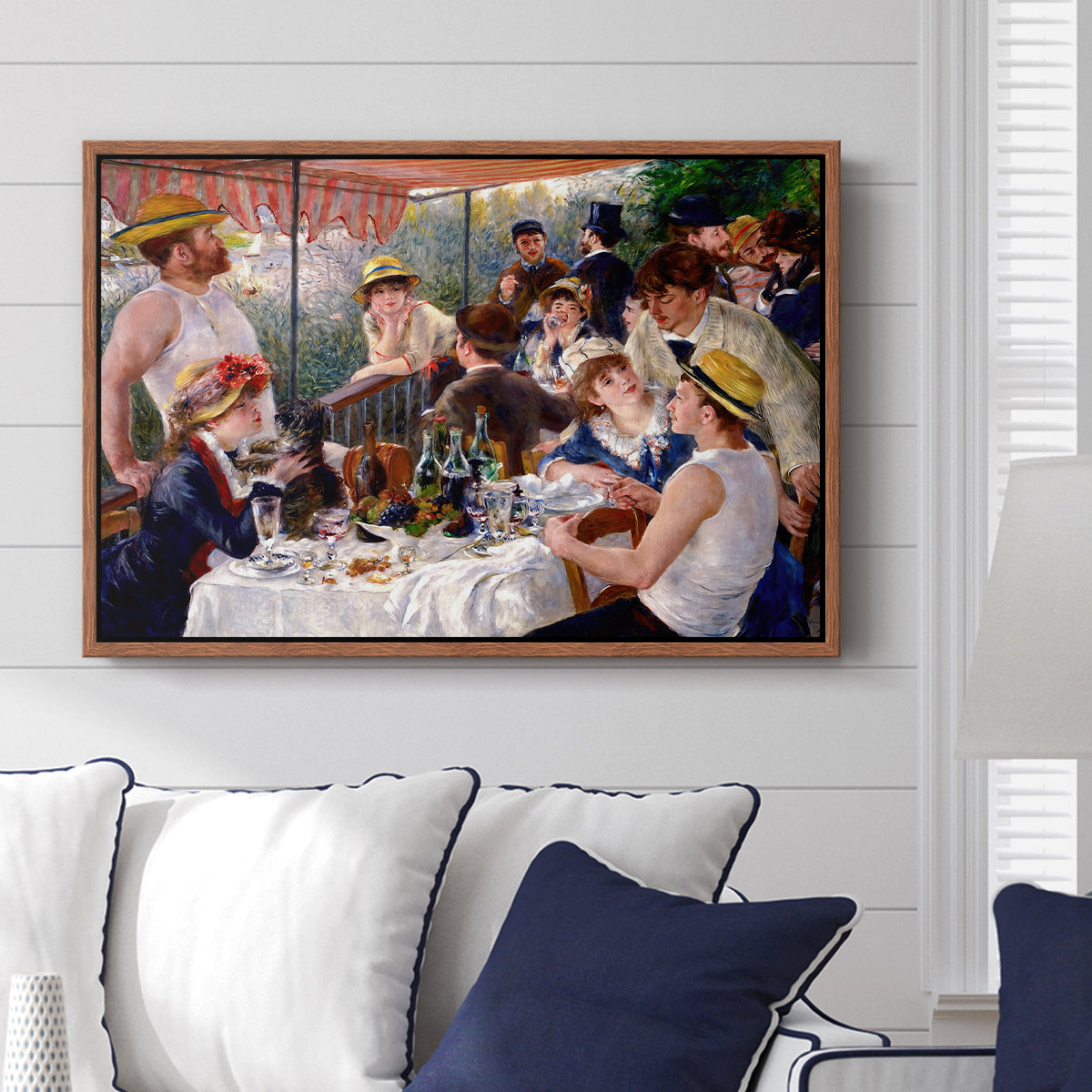 Luncheon of the Boating Party (Le Déjeuner des canotiers), 1880-1881 by Pierre-Auguste Renoir displayed above a sofa in a living room in a walnut floater frame, featuring a lively gathering of men and women eating and socializing at outdoor table.