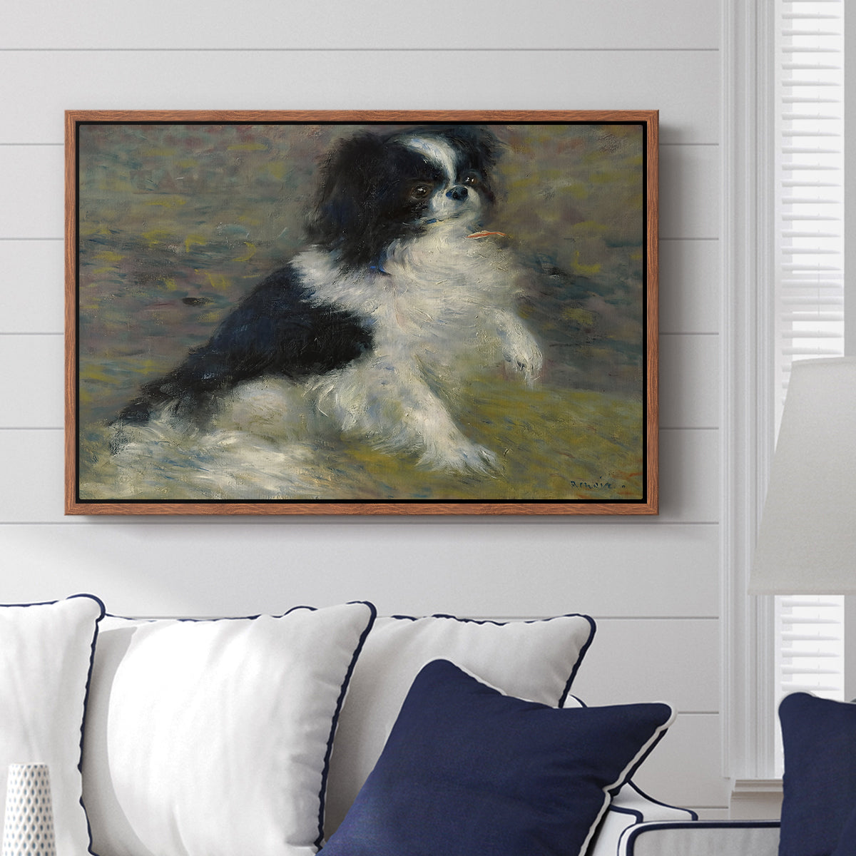 Tama, the Japanese Dog, c. 1876 by Pierre-Auguste Renoir displayed above a sofa in a living room in a walnut floater frame, featuring an impressionist painting of a dog wading through water with blurred background.