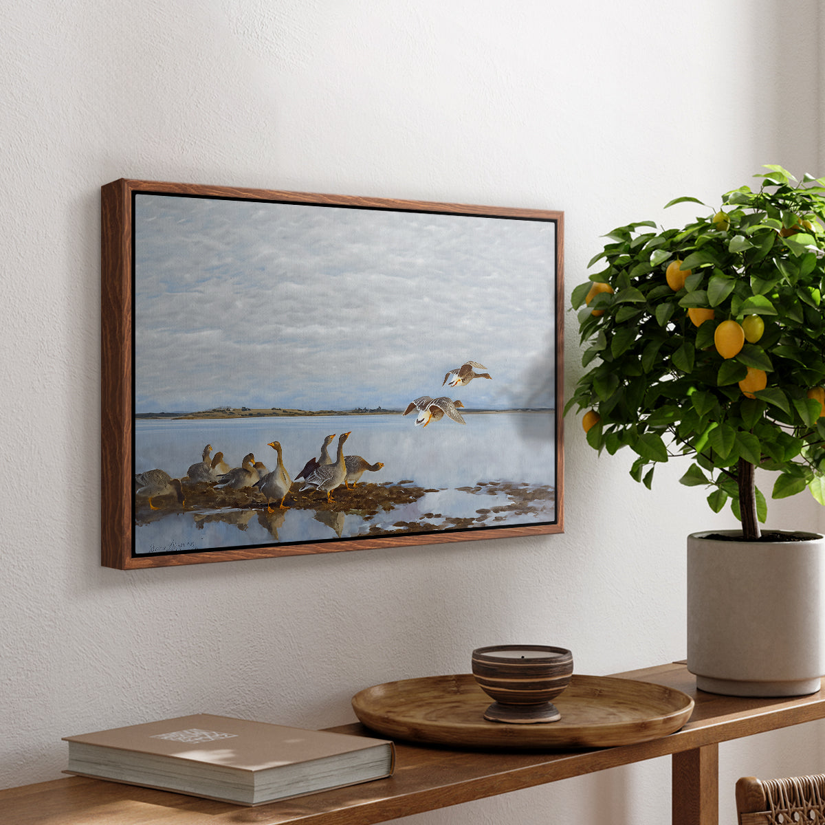 Greylag Geese (Grågäss), 1922 by Bruno Liljefors, presented in a walnut floater framed canvas featuring a group of geese gathered near water in a natural wetland landscape, displayed above a hallway console table.