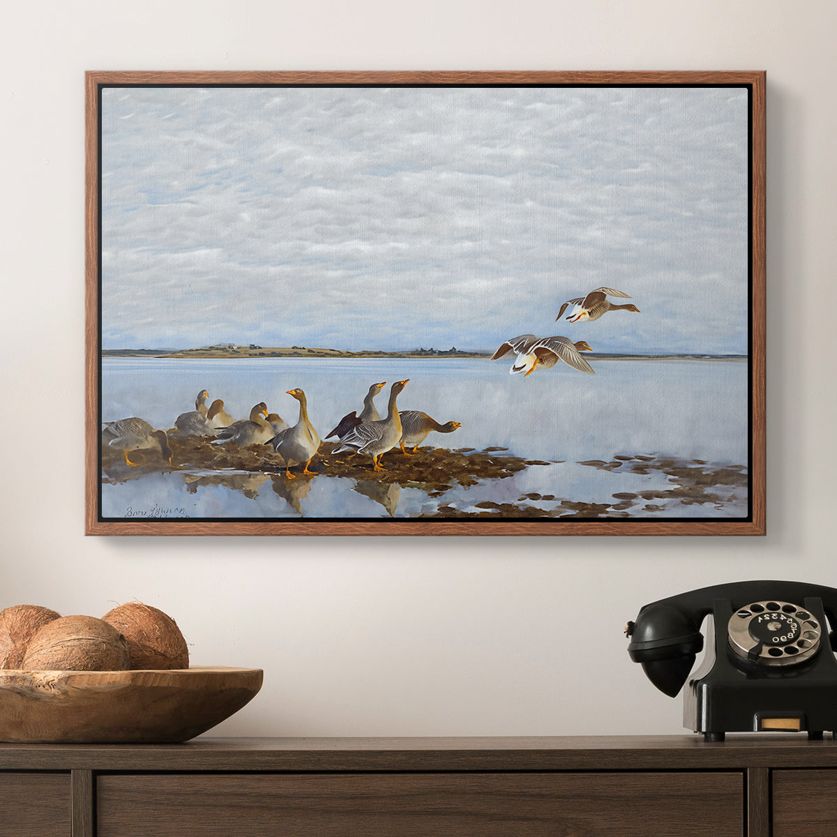 Greylag Geese (Grågäss), 1922 by Bruno Liljefors in a walnut floater framed canvas displayed above a console table in a hallway, featuring a flock of geese positioned along marshy terrain.