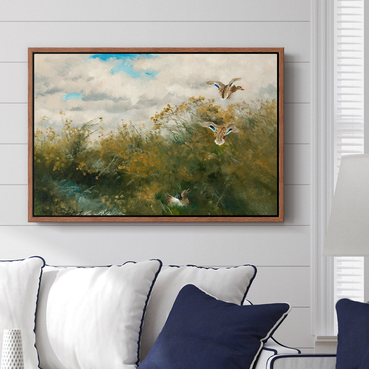Wild Ducks (Grasänder), 1890 by Bruno Liljefors displayed above a sofa in a living room in a walnut floater frame, featuring a wildlife scene of ducks walking through tall grass beside water.