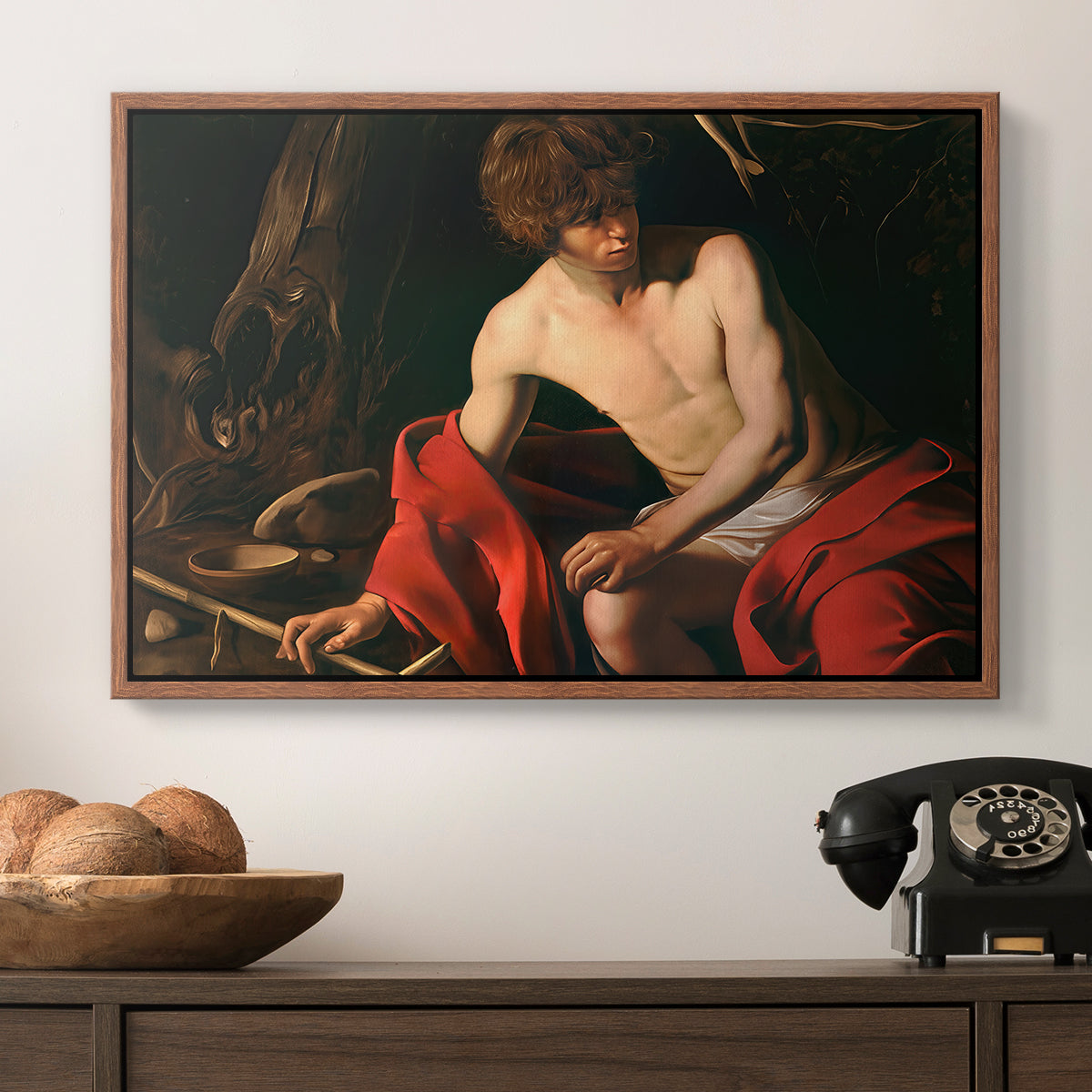 Saint John the Baptist in the Wilderness, c. 1603-1604 by Caravaggio in a walnut floater framed canvas displayed above a console table in a hallway, featuring a contemplative religious figure in rustic wilderness environment.