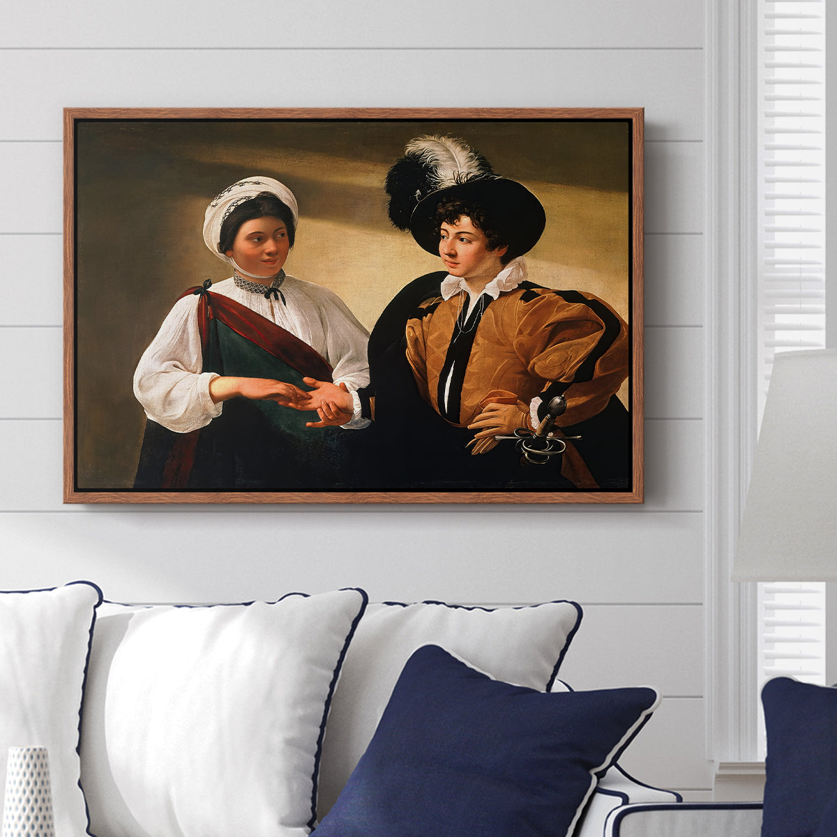 The Fortune Teller (Louvre Version), c. 1595 by Caravaggio displayed above a sofa in a living room in a walnut floater frame, featuring a fortune teller examining hand of man as she slyly removes his ring.