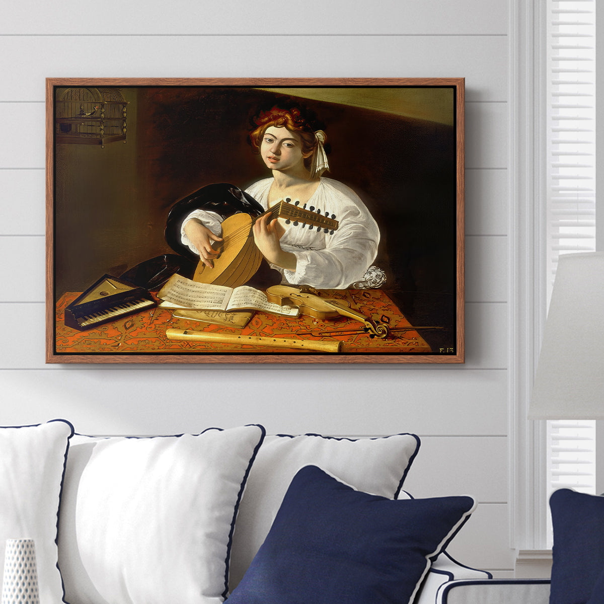 The Lute Player (Wildenstein Version), c. 1596 by Caravaggio displayed above a sofa in a living room in a walnut floater frame, featuring a musician seated with lute and musical instruments on table.