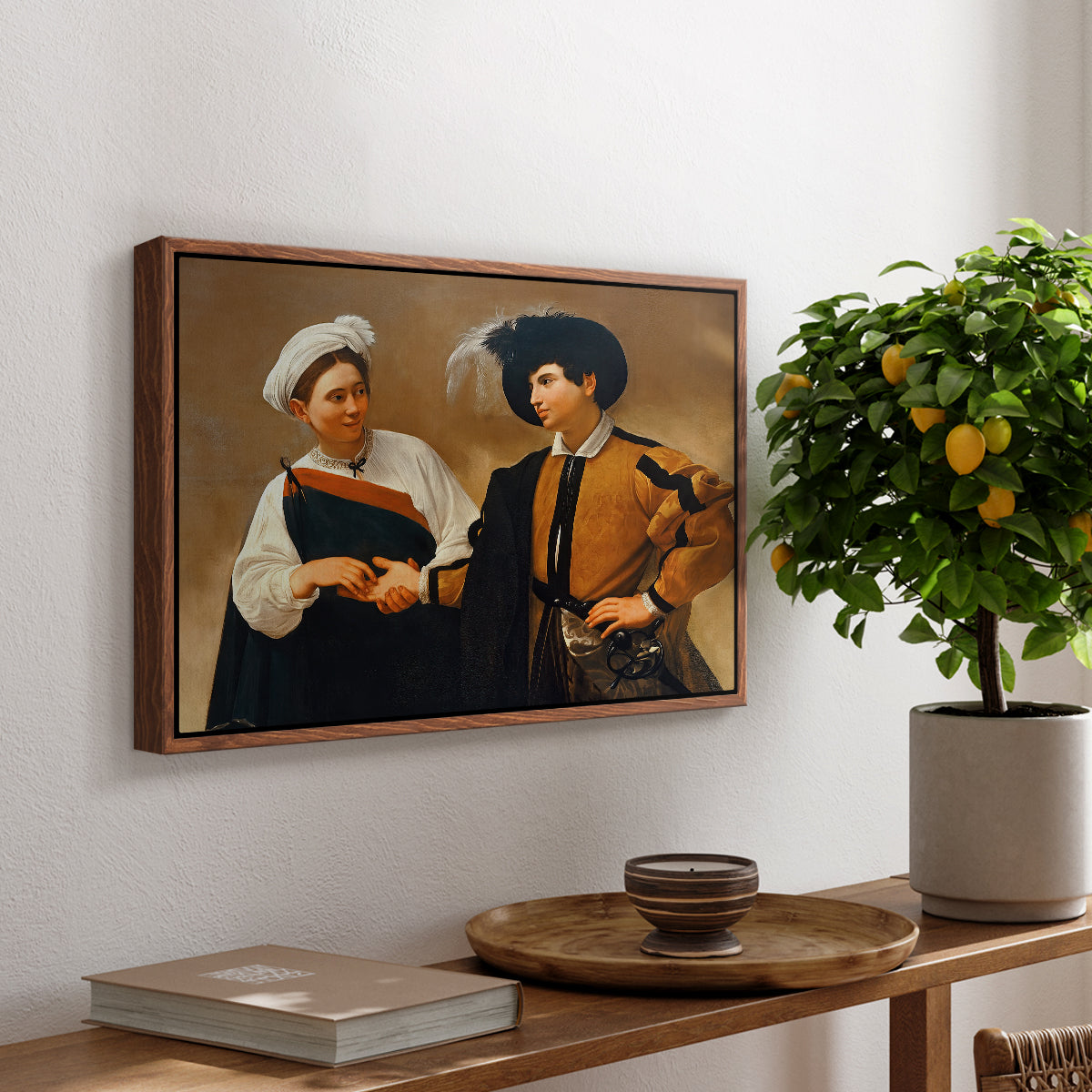 The Fortune Teller (Capitoline Version), c. 1599 by Caravaggio, presented in a walnut floater framed canvas featuring a woman reading man's palm while discreetly removing his ring, displayed above a hallway console table.