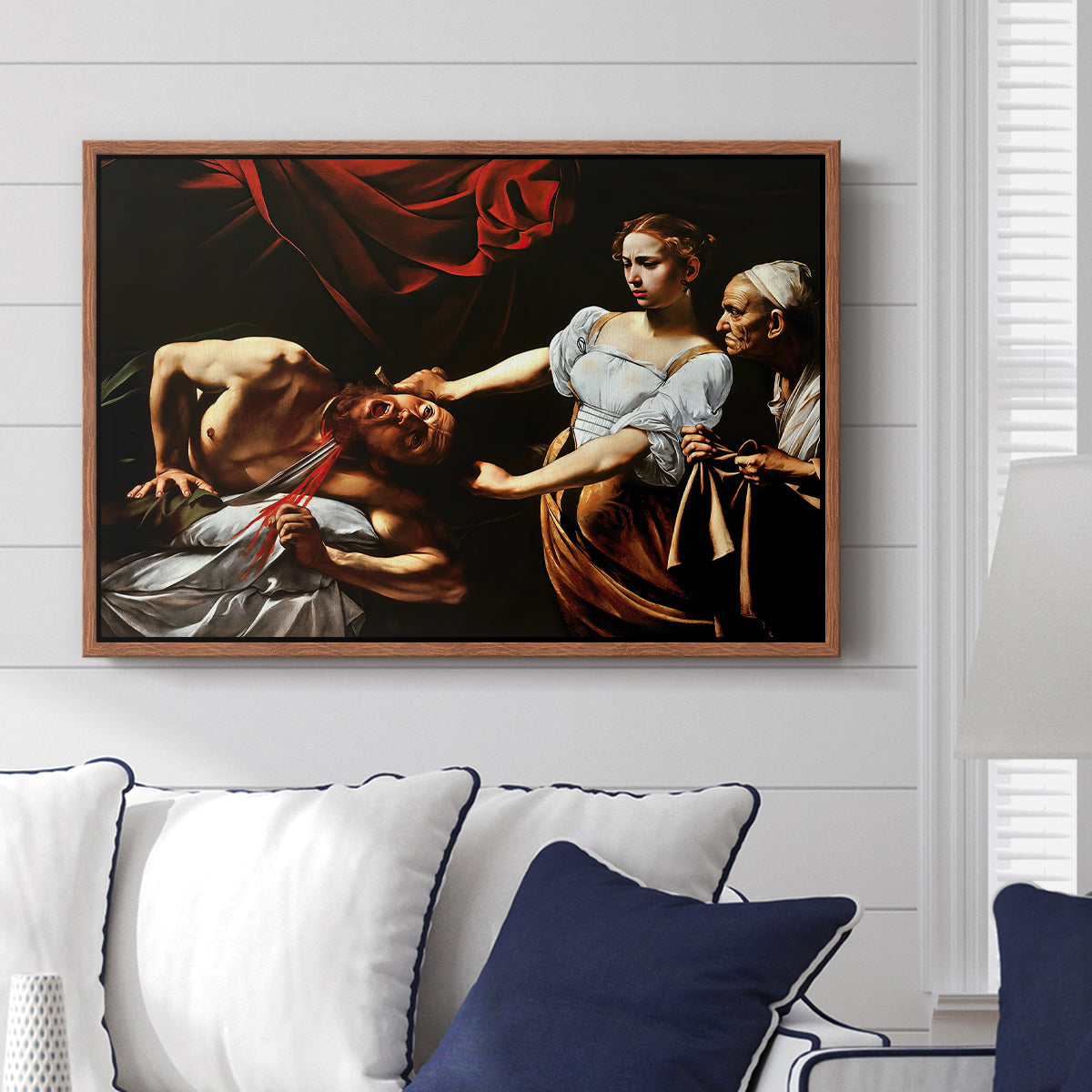 Judith Beheading Holofernes, c. 1599 by Caravaggio displayed above a sofa in a living room in a walnut floater frame, featuring a dramatic biblical scene of woman beheading man in bed.