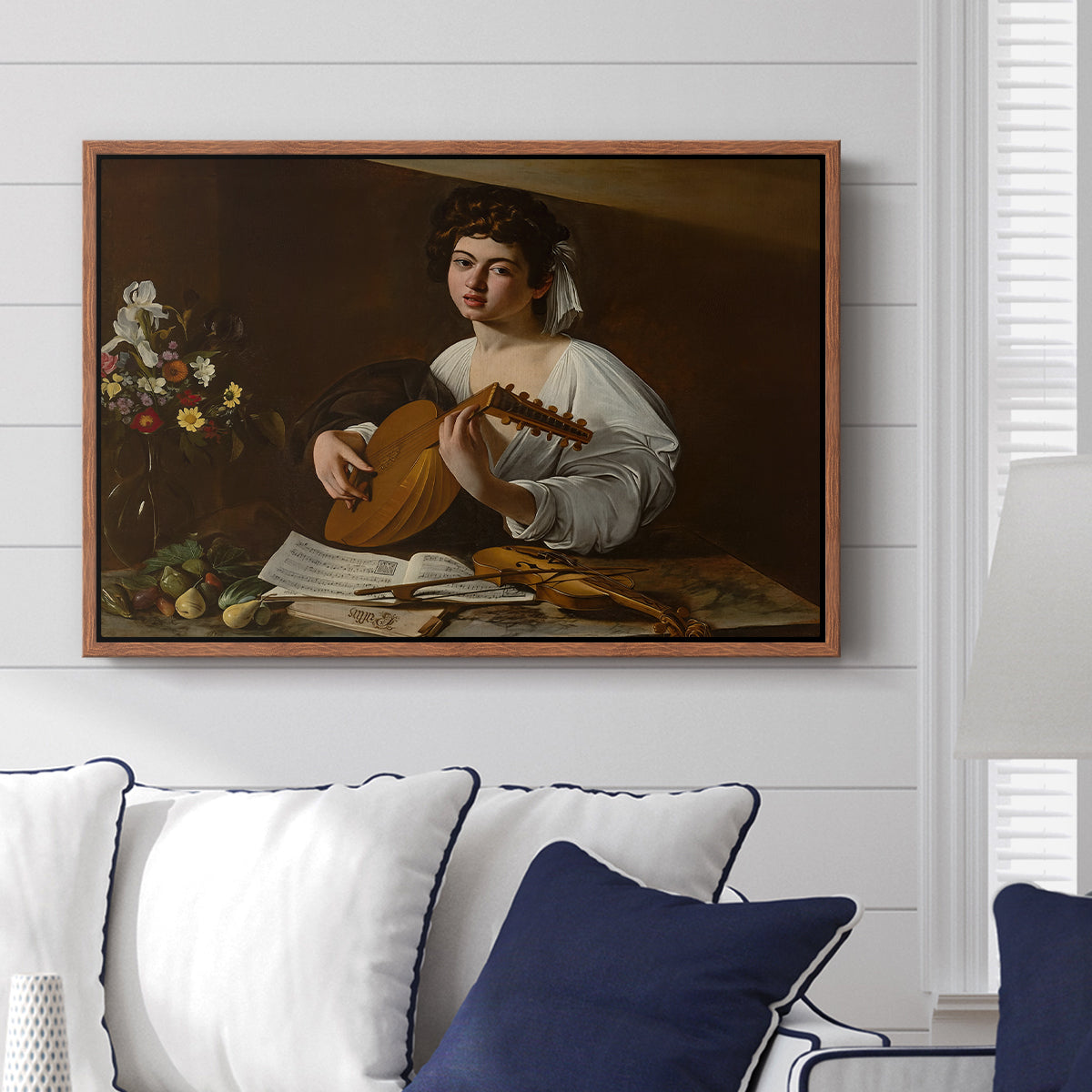 The Lute Player (Hermitage Version), c. 1596 by Caravaggio displayed above a sofa in a living room in a walnut floater frame, featuring a portrait of lute player surrounded by still life arrangement.