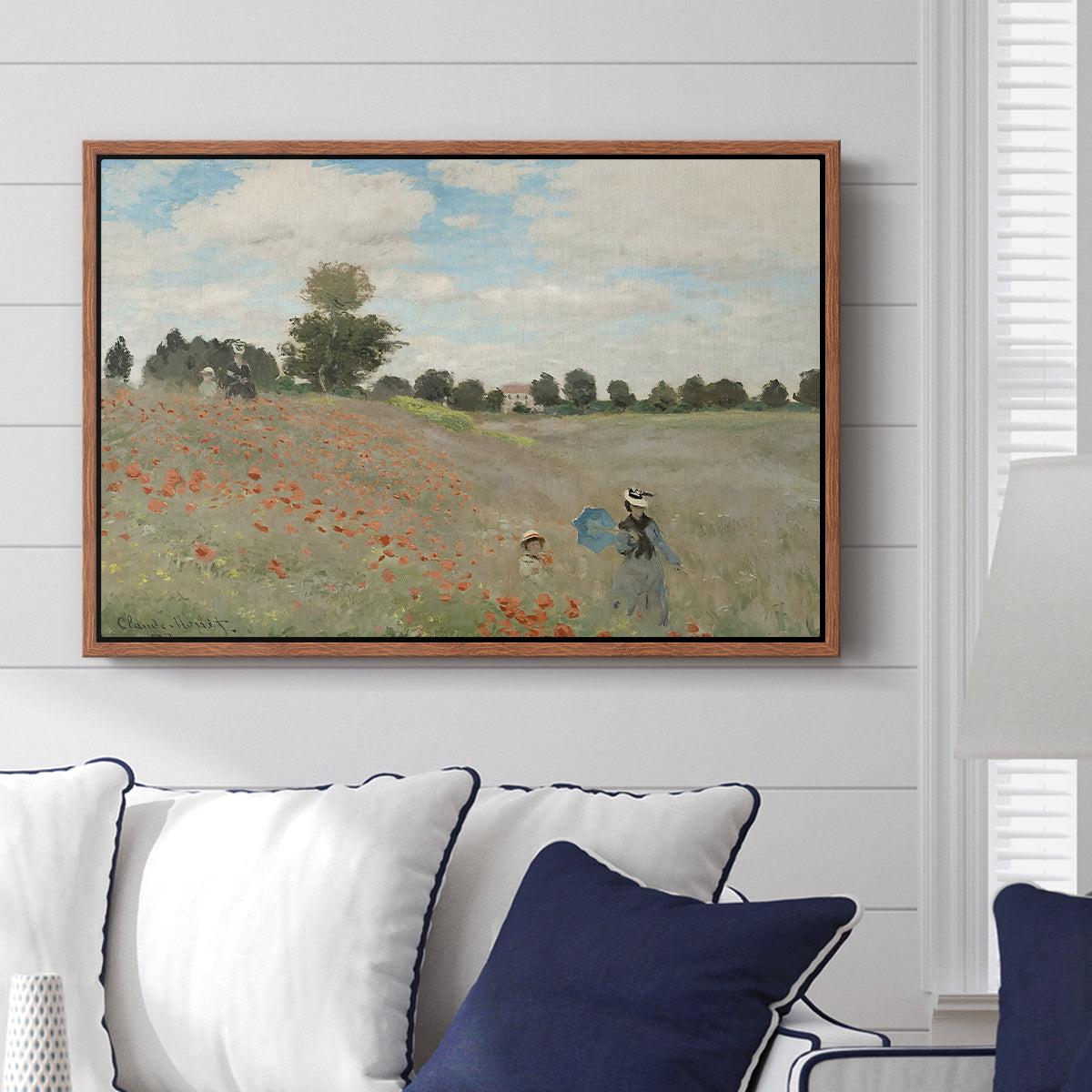 The Poppy Field near Argenteuil, 1873 by Claude Monet displayed above a sofa in a living room in a walnut floater frame, featuring an impressionist countryside scene with flowers and strolling figures.