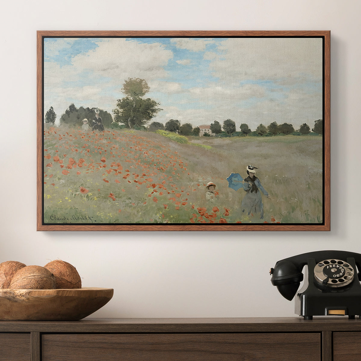 The Poppy Field near Argenteuil, 1873 by Claude Monet in a walnut floater framed canvas displayed above a console table in a hallway, featuring a rural landscape with scattered figures among blooming flowers.
