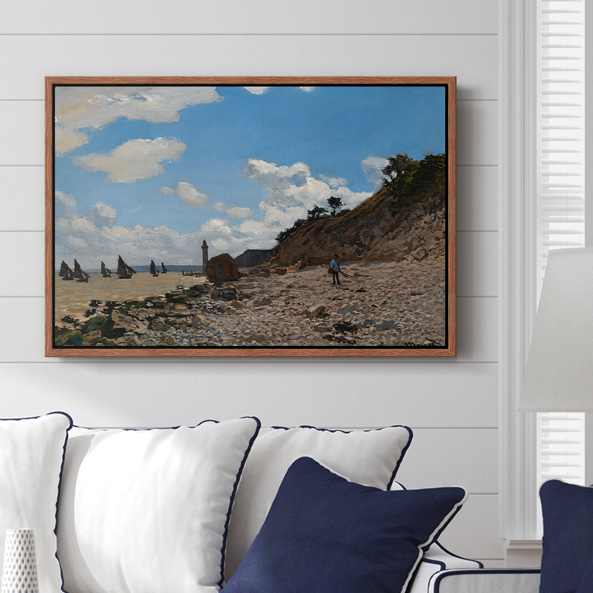 The Beach at Honfleur, 1864 by Claude Monet displayed above a sofa in a living room in a walnut floater frame, featuring an impressionist seaside with people and sailboats under bright sky.